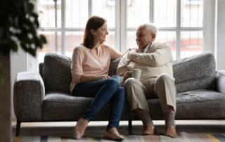 Adult woman drinks tea alongside senior man on couch.