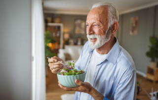 Senior man eating a salad while looking out a window.